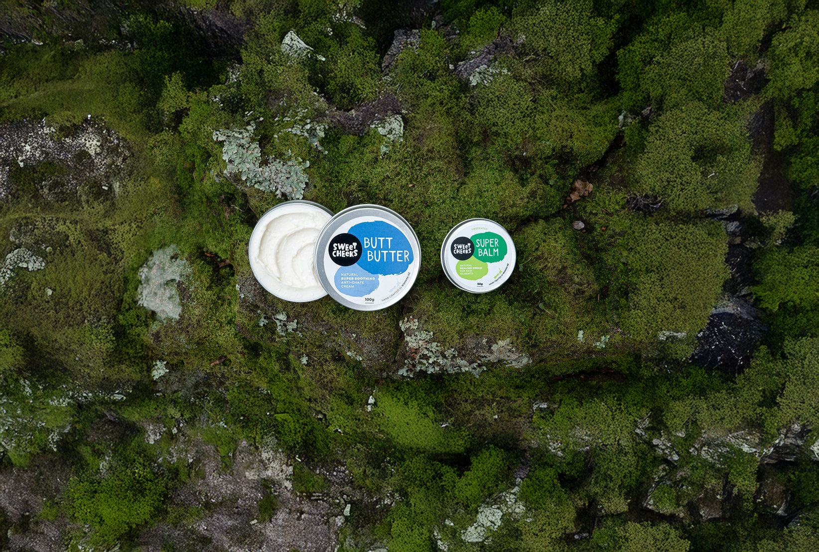 Three containers of 'Butt Butter' on a mossy rock surface