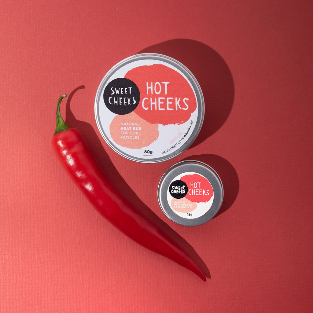 Two tins of 'Sweet Cheeks Hot Cheeks' product with a red chili pepper on a red background