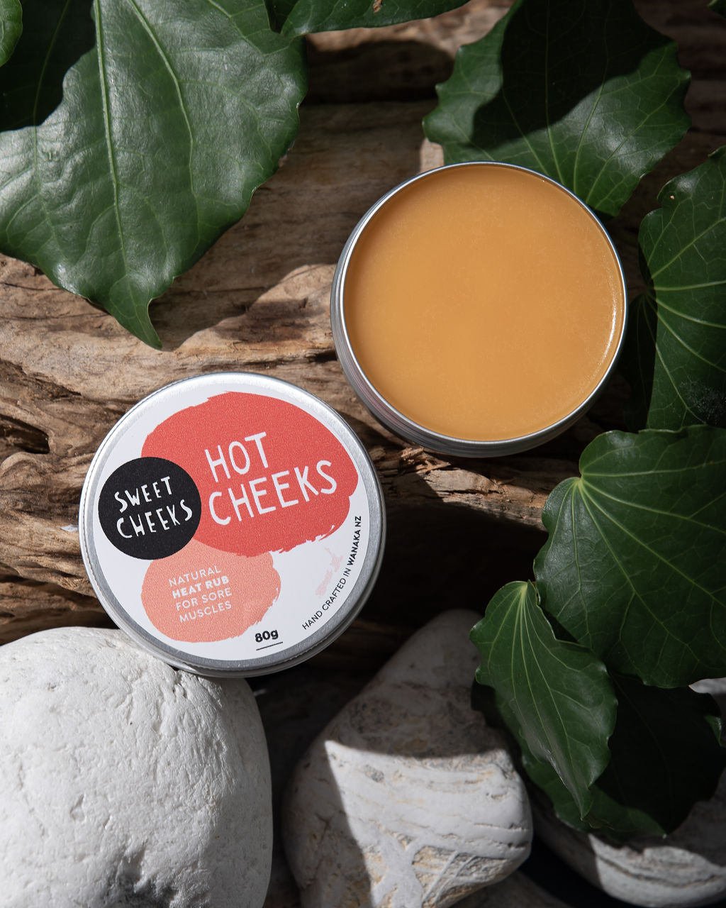 One open tin  of 'Sweet Cheeks Hot Cheeks' product on a natural background with leaves.