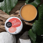 One open tin  of 'Sweet Cheeks Hot Cheeks' product on a natural background with leaves.